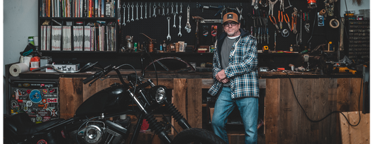 Steve Gerow, artist and co-founder of The Creative Company, standing in his workshop surrounded by an array of tools, a motorcycle, and shelves filled with books and boxes